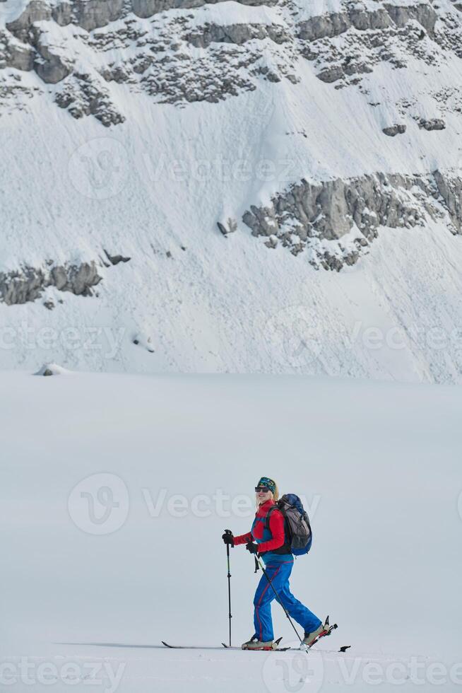 A female skier stands at the snowy summit of a mountain, equipped with professional gear and skis, poised for an exhilarating descent. photo