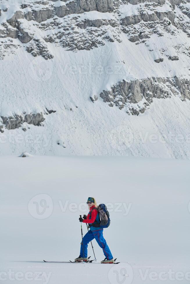 A female skier stands at the snowy summit of a mountain, equipped with professional gear and skis, poised for an exhilarating descent. photo