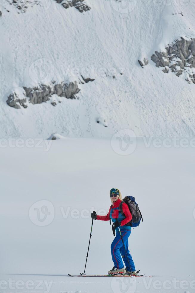 A female skier stands at the snowy summit of a mountain, equipped with professional gear and skis, poised for an exhilarating descent. photo