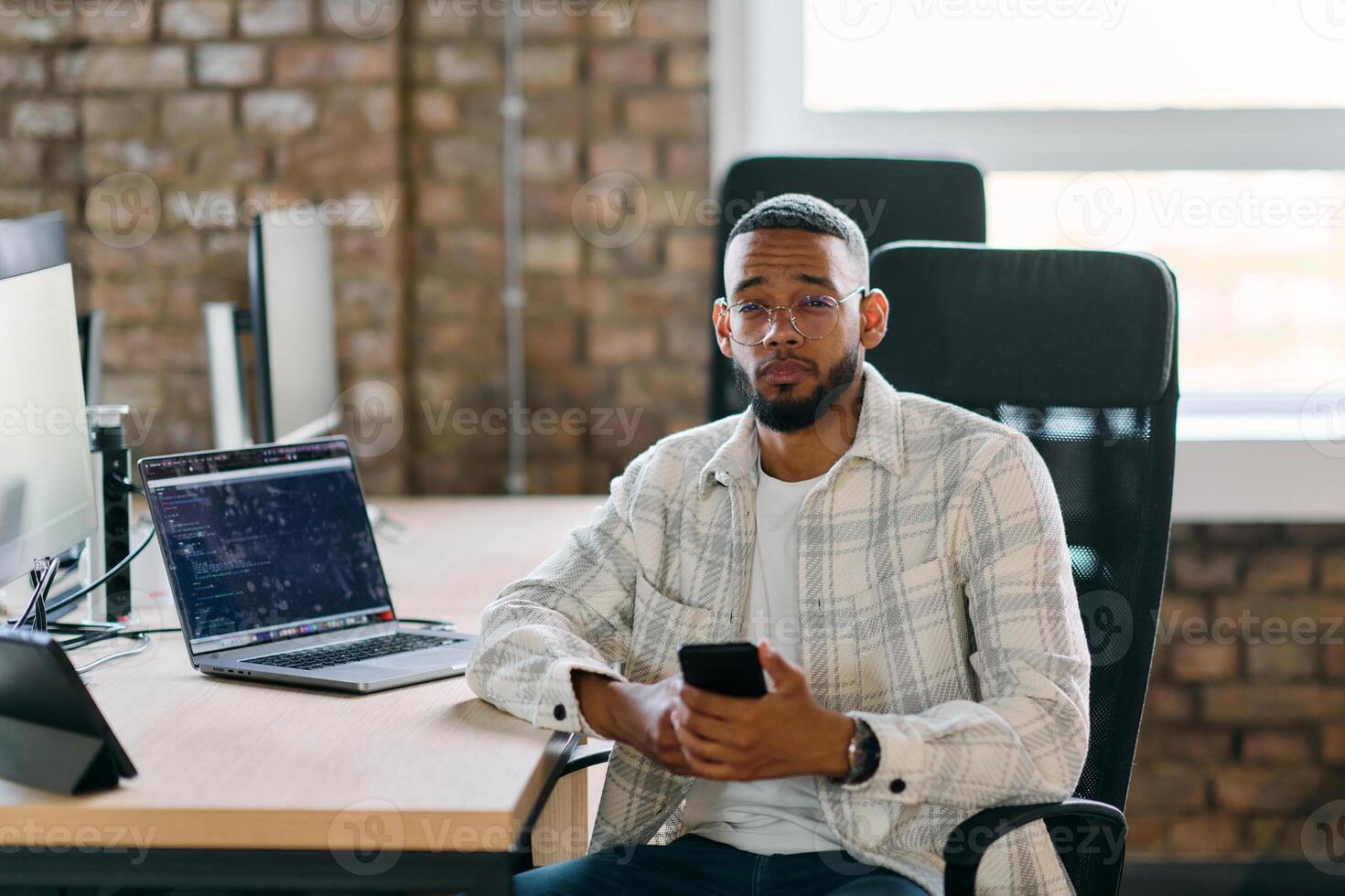 African American entrepreneur takes a break in a modern office, using a smartphone to browse social media, capturing a moment of digital connectivity and relaxation amidst his business endeavors. photo