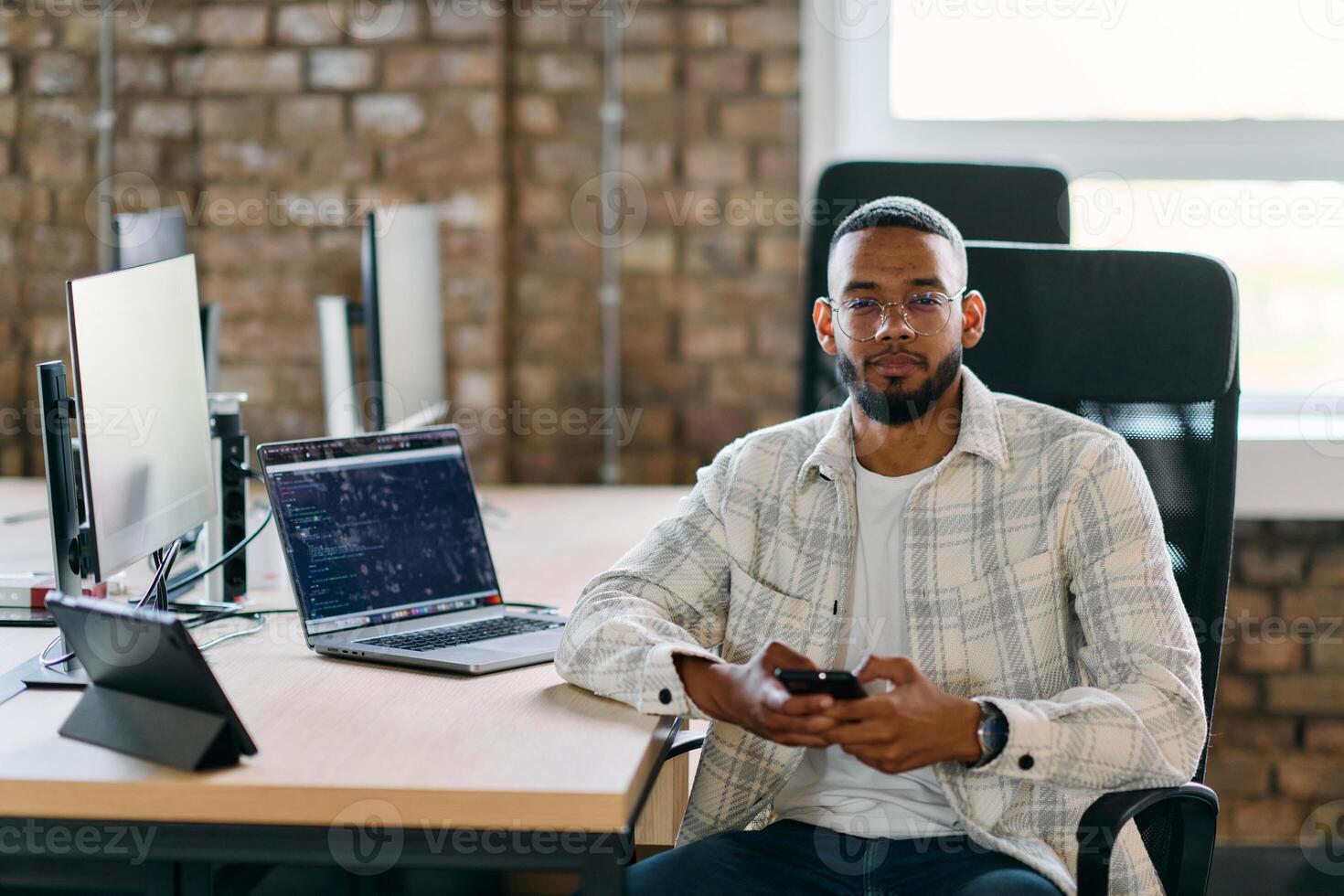 African American entrepreneur takes a break in a modern office, using a smartphone to browse social media, capturing a moment of digital connectivity and relaxation amidst his business endeavors. photo