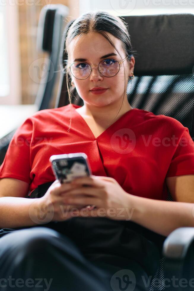 A businesswoman resting on a short break from work in a modern startup coworking center, using her smartphone to unwind and recharge photo