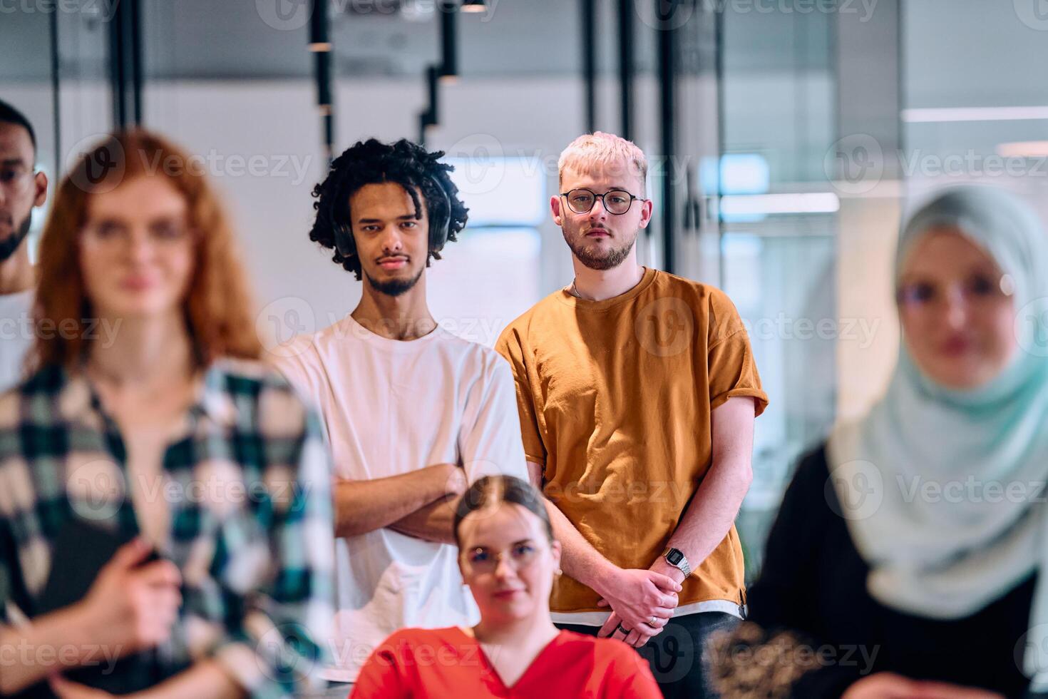 A diverse group of young business people walking a corridor in the glass-enclosed office of a modern startup, including a person in a wheelchair and a woman wearing a hijab photo