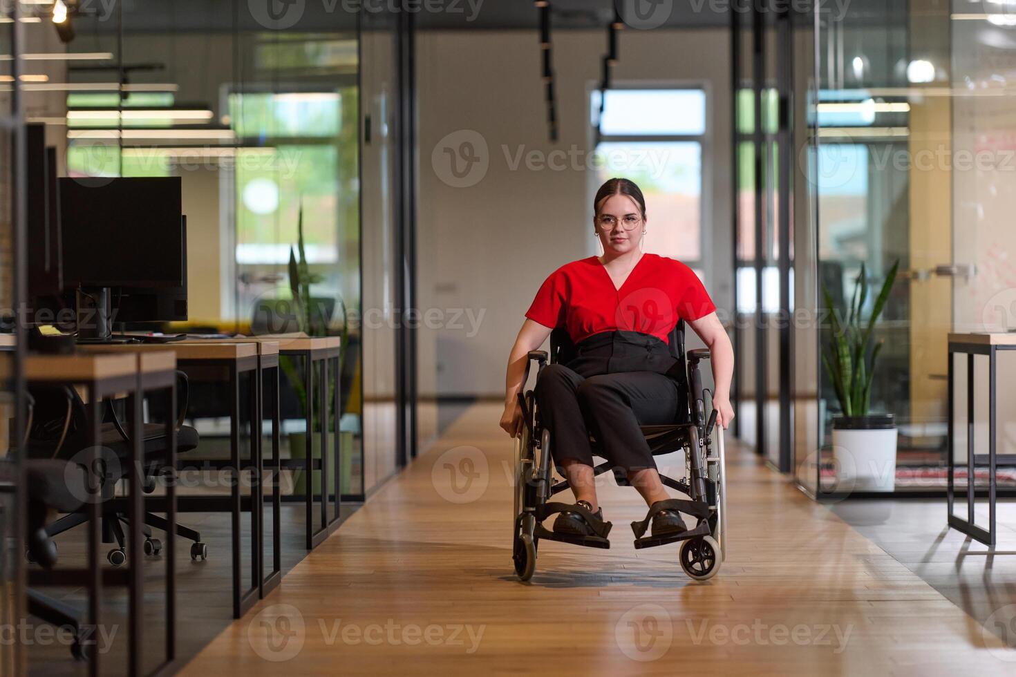A modern young businesswoman in a wheelchair is surrounded by an inclusive workspace with glass-walled offices, embodying determination and innovation in the business world photo