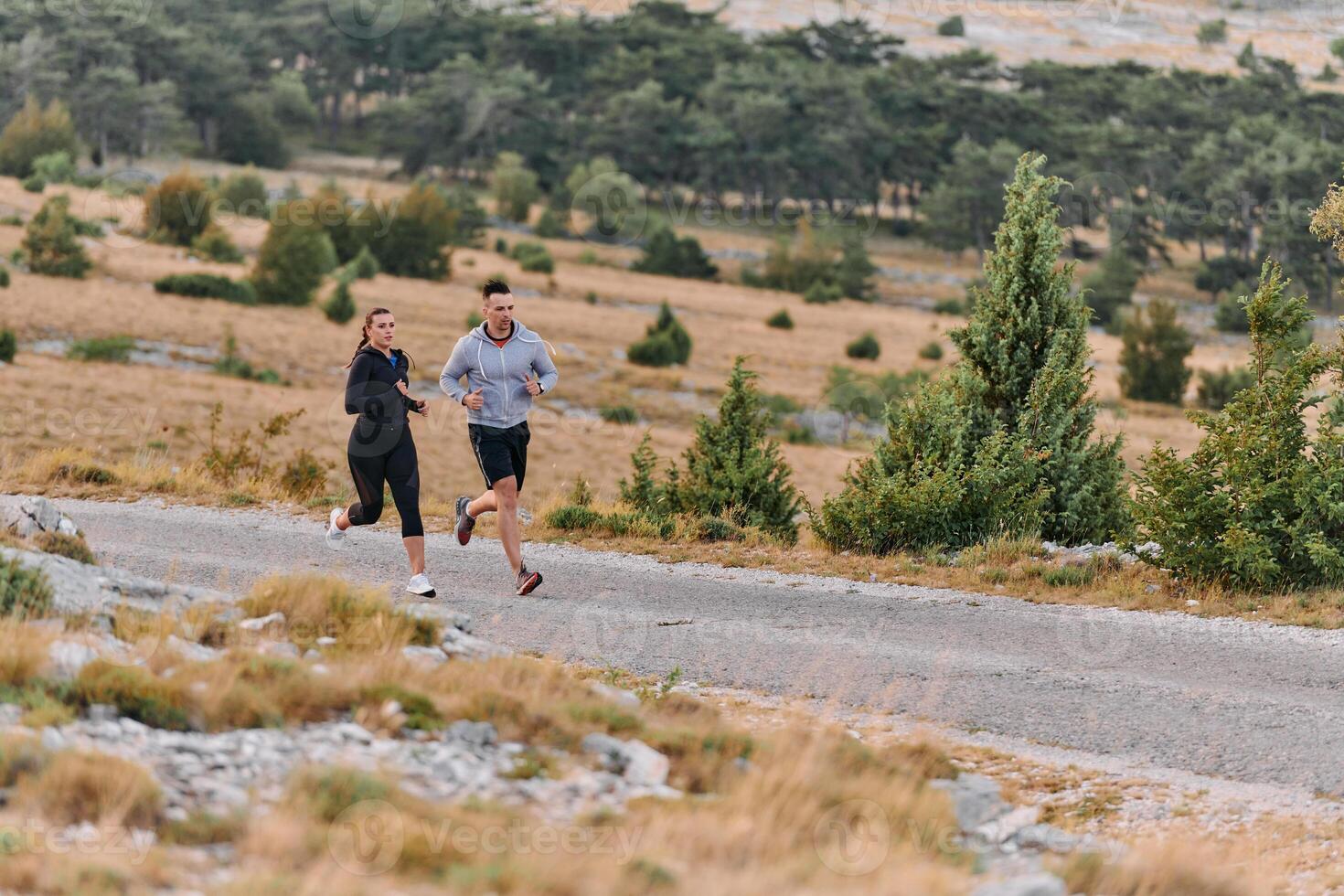 A couple dressed in sportswear runs along a scenic road during an early morning workout, enjoying the fresh air and maintaining a healthy lifestyle photo