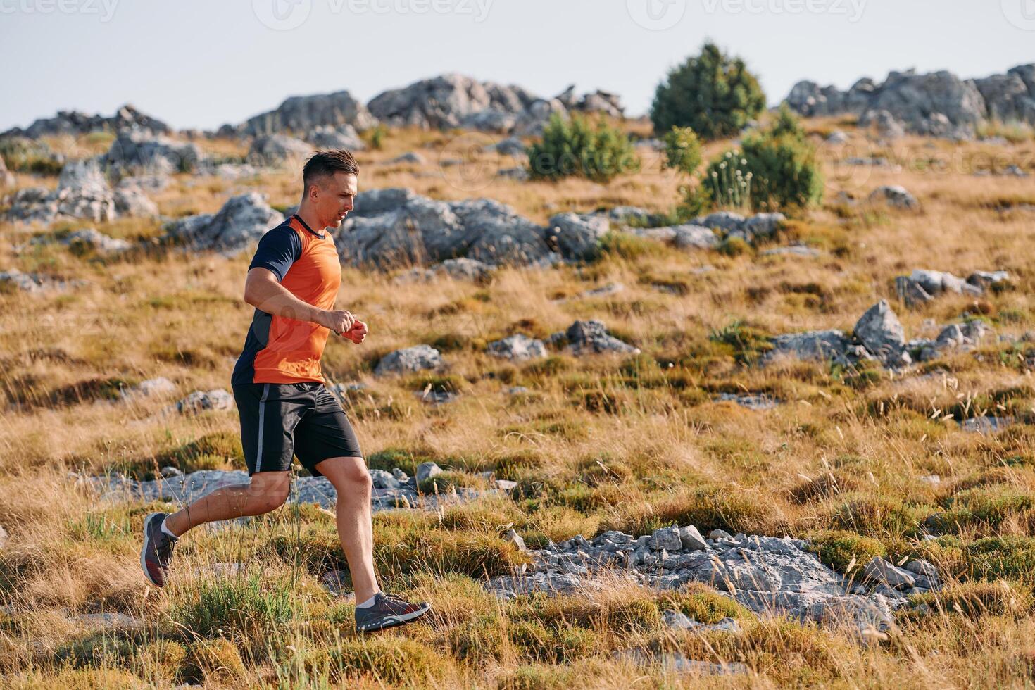 Determined Athlete Running Through Rugged Mountain Terrain at Sunrise. photo