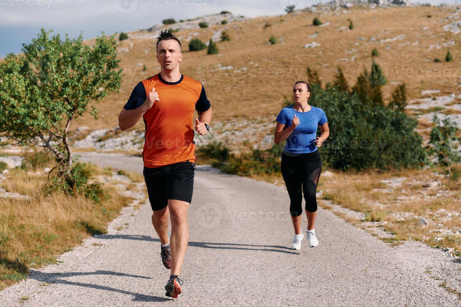 A couple dressed in sportswear runs along a scenic road during an early morning workout, enjoying the fresh air and maintaining a healthy lifestyle photo