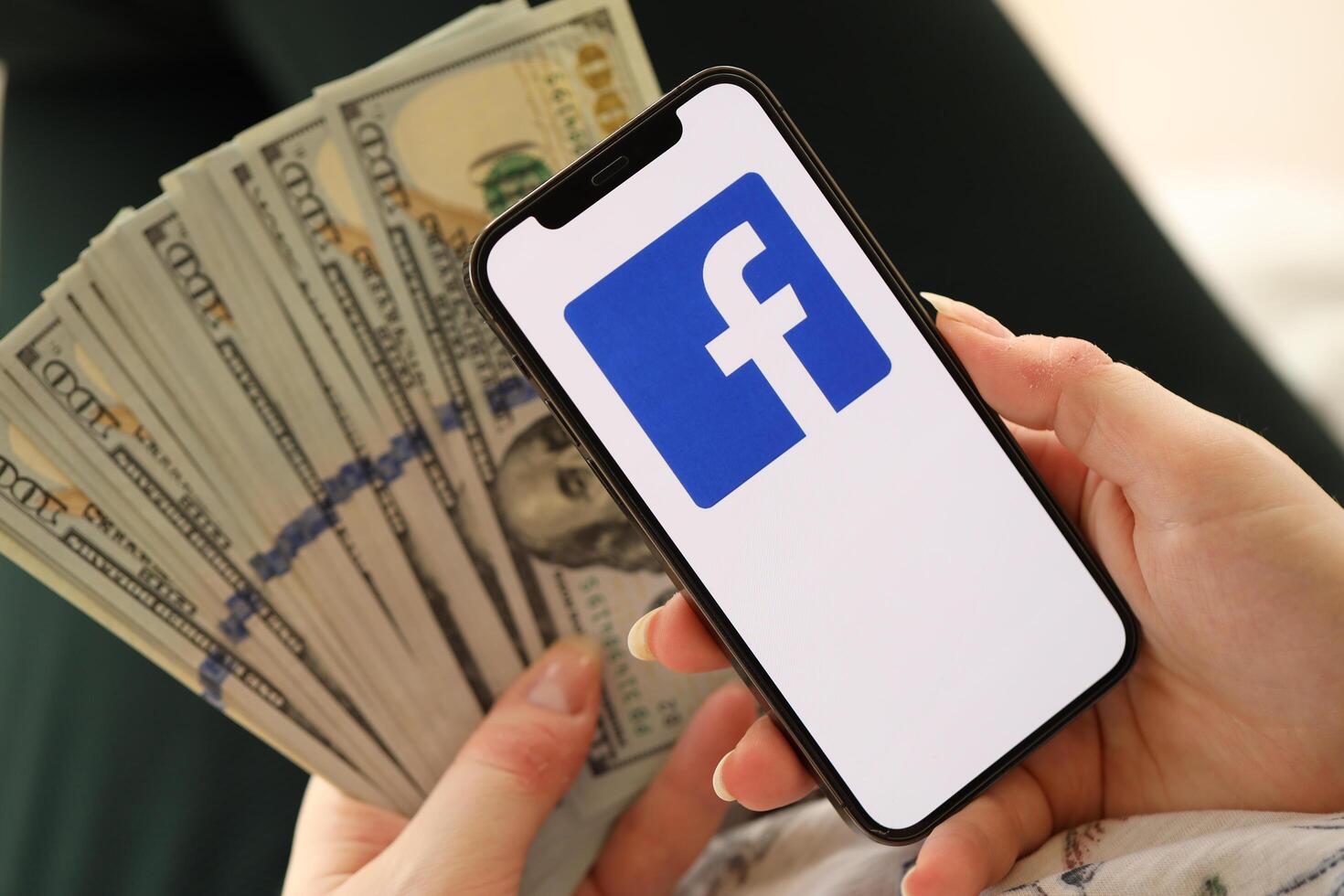 KYIV, UKRAINE - APRIL 1, 2024 Facebook icon on smartphone screen and money in female hand photo