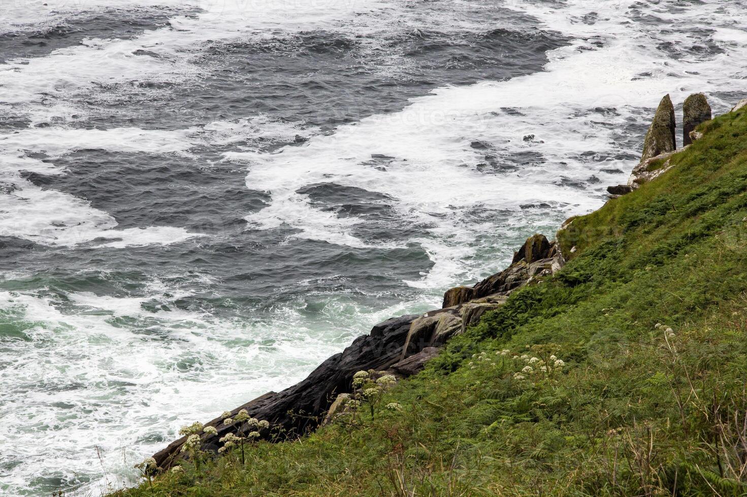 Rough Seas Crashing Against Green Cliffs on a Cloudy Day, in Ireland photo