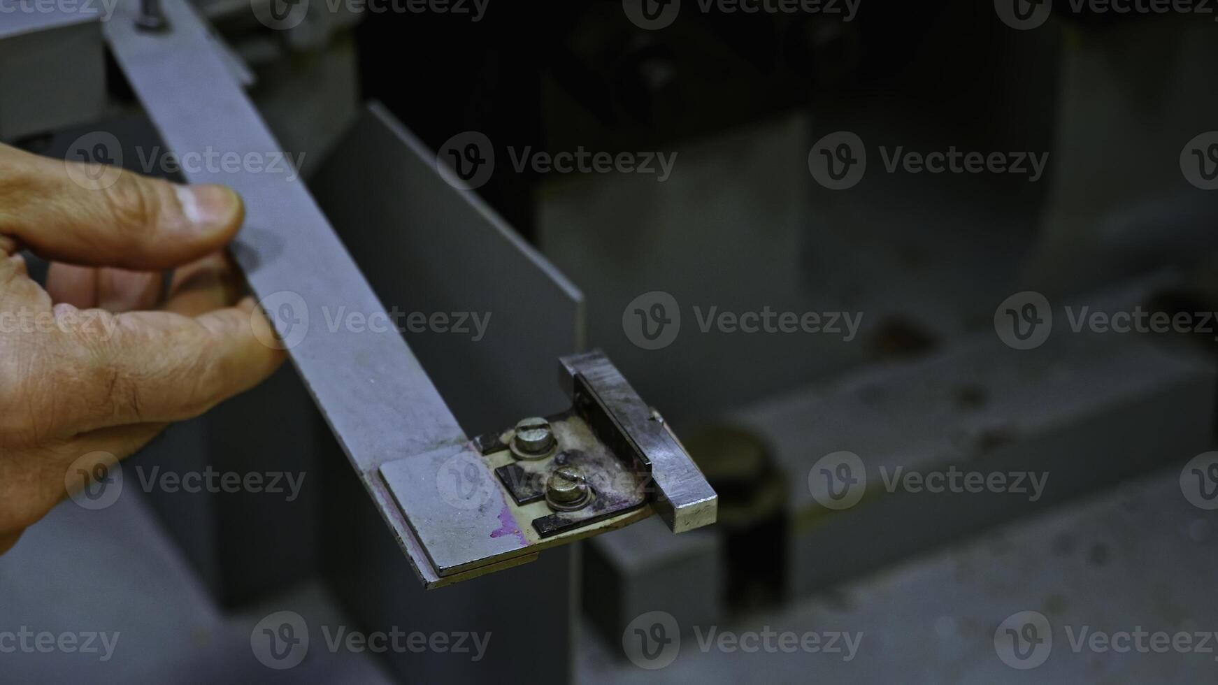 Close up of worker hands putting small metal tile for processing in industrial machine. Stock footage. Details of workshop. photo