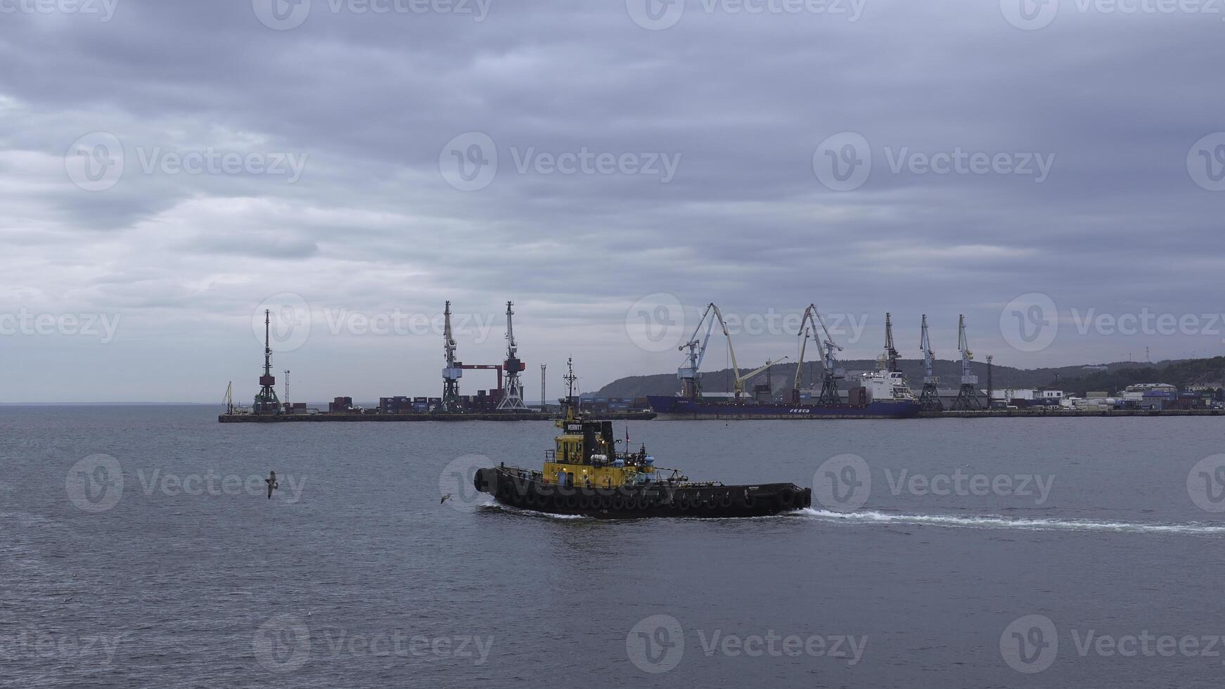 Fishing boat on background of port in cloudy weather. Clip. Fishing vessel sails out of seaport into sea. Fishing boat sails into sea on cloudy day photo