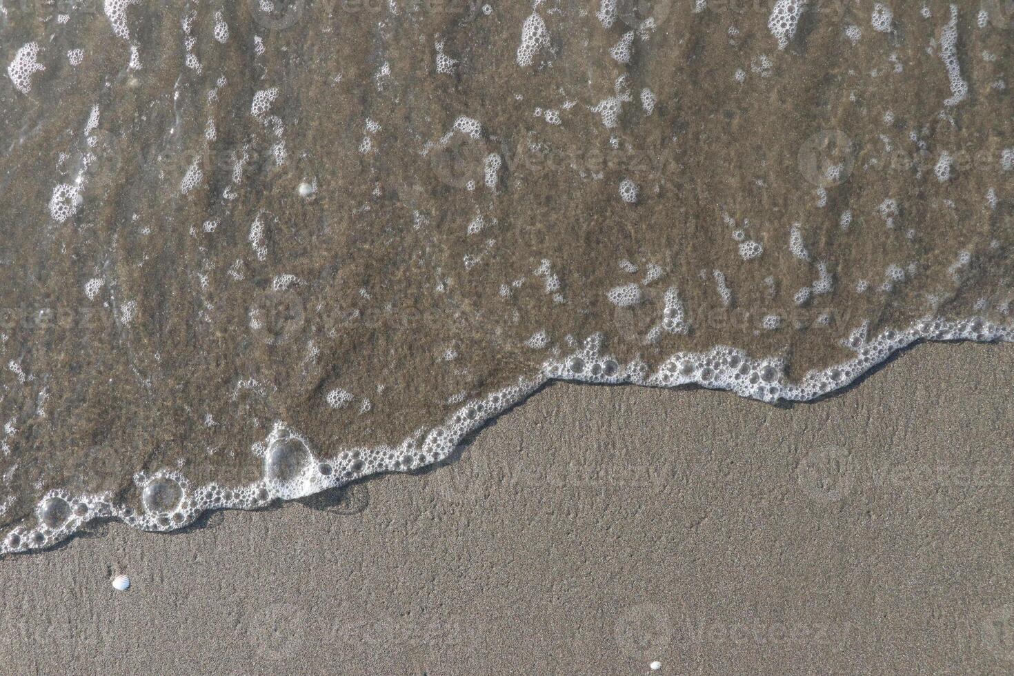 The calm wave of the sea with foam on the beach sand photo