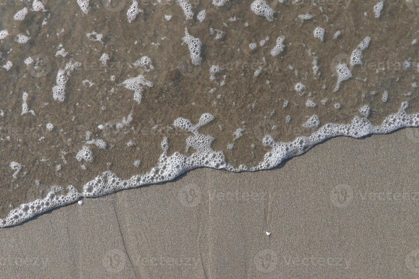 The calm wave of the sea with foam on the beach sand photo
