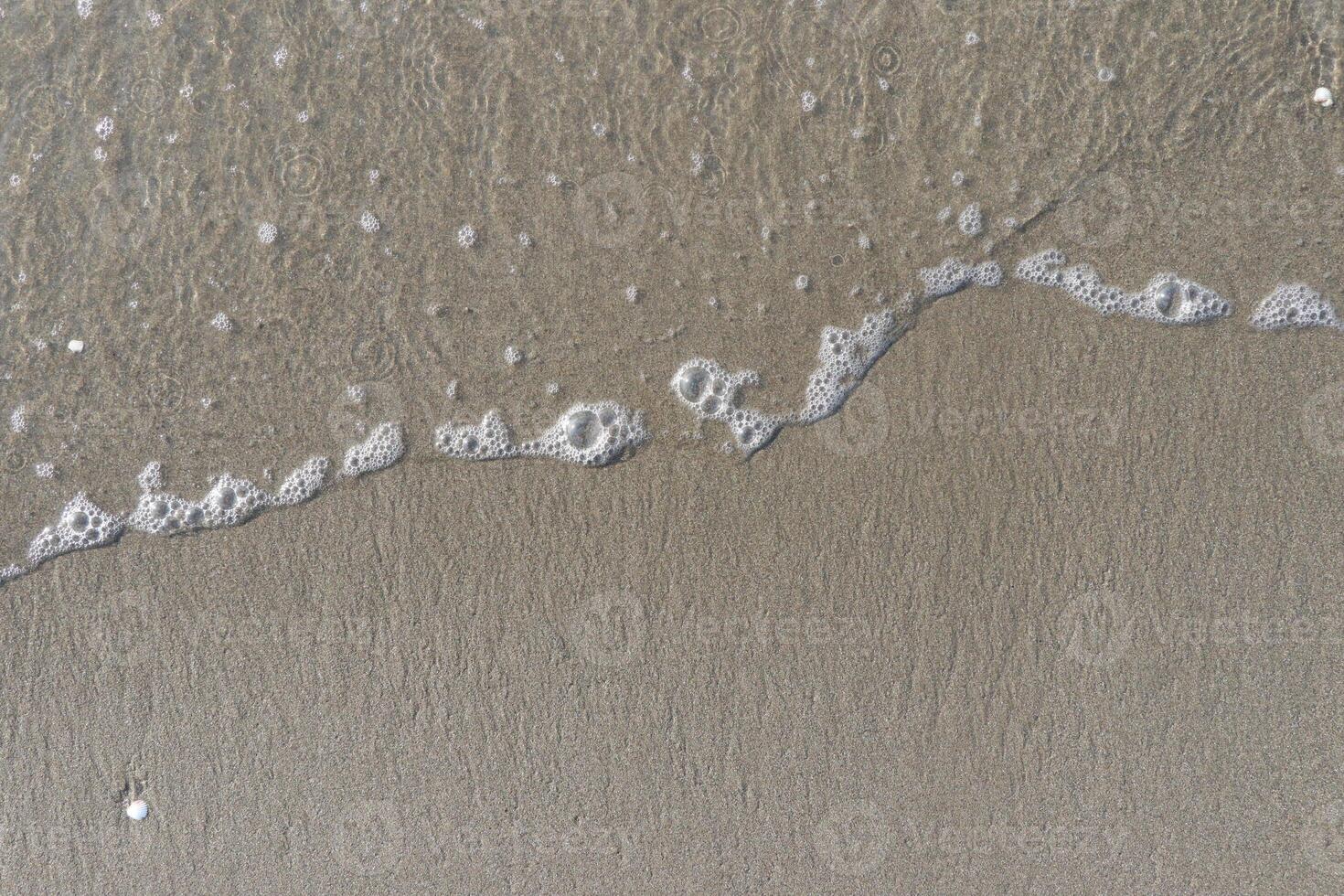 The calm wave of the sea with foam on the beach sand photo