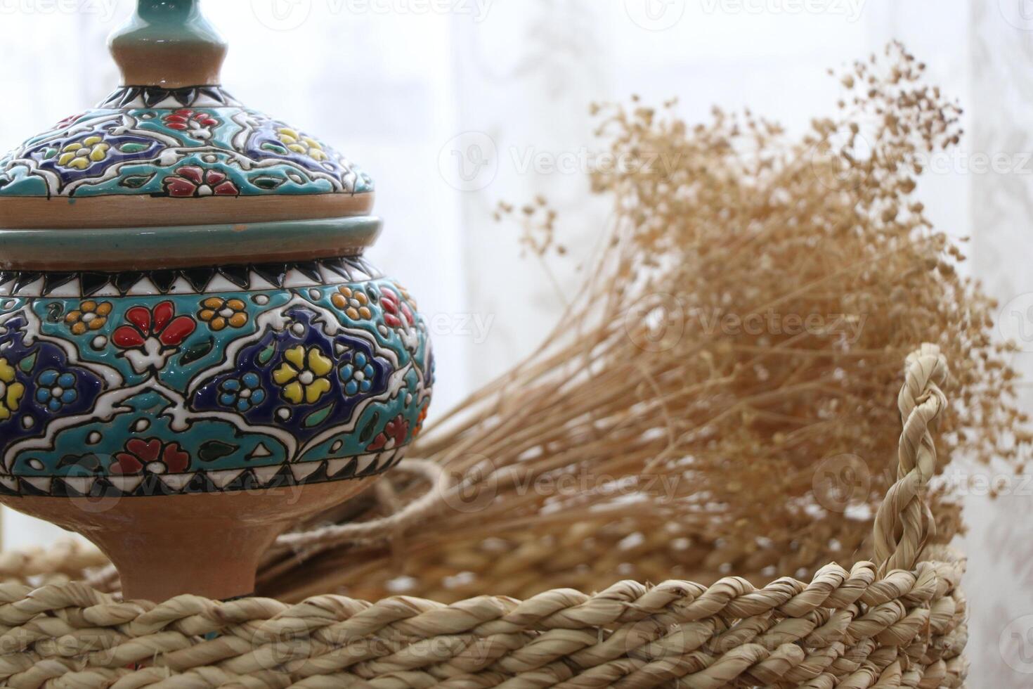 Dry flax plant and traditional painted vase on a wicker basket - Minimal decorative items photo