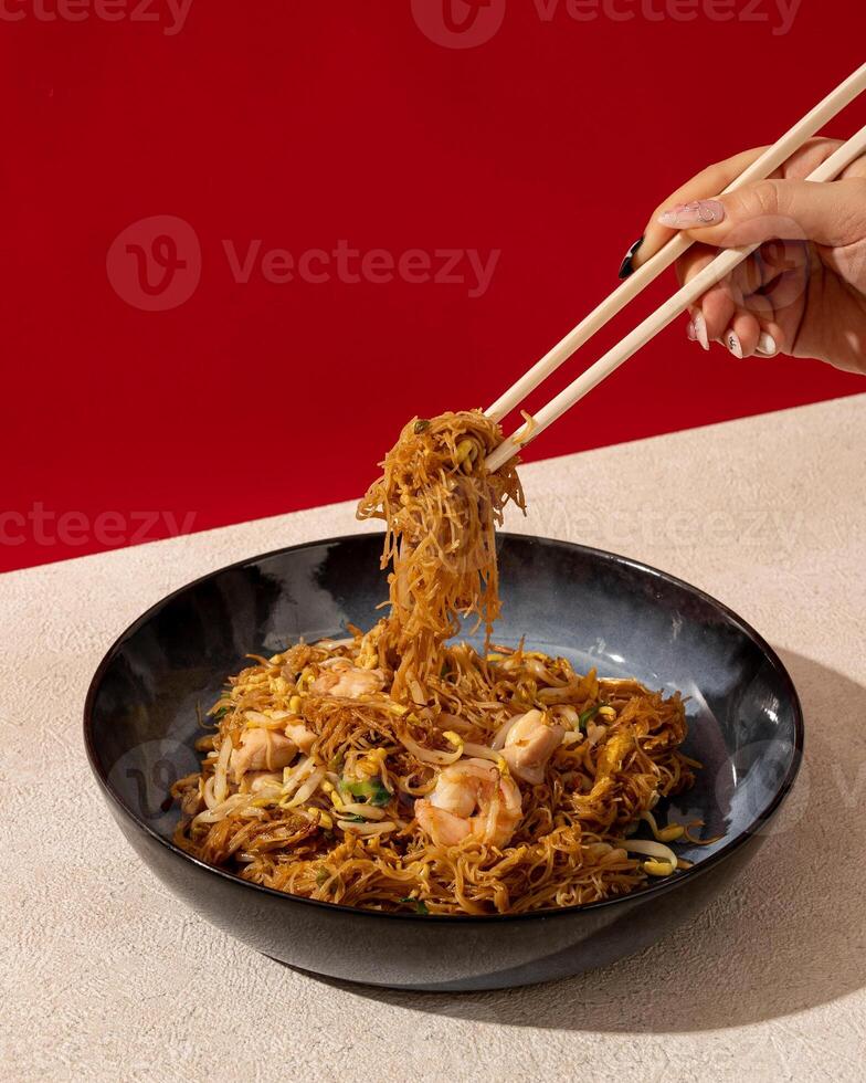 asiático arroz tallarines con camarón y vegetales de cerca en el mesa con blanco y rojo antecedentes color. chino comida menú foto