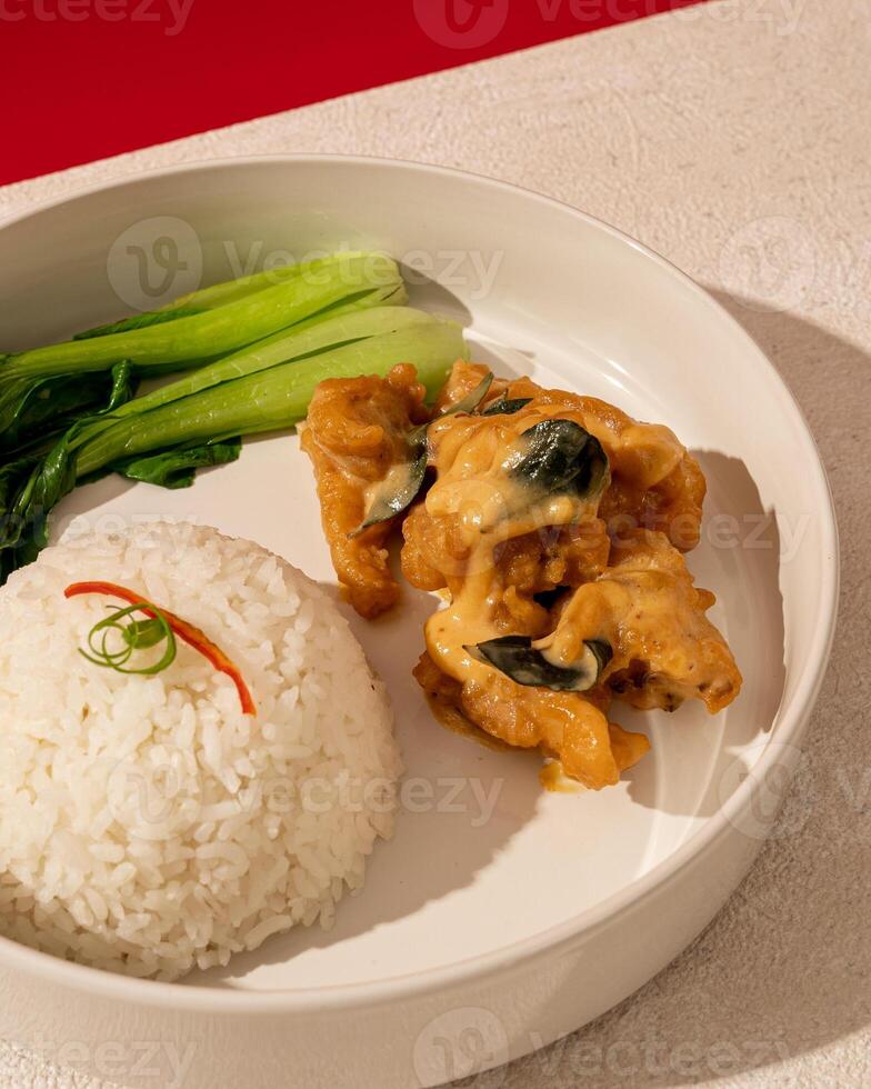 The combination of soft salted egg sauce and crunchy fried chicken is served with warm rice photo