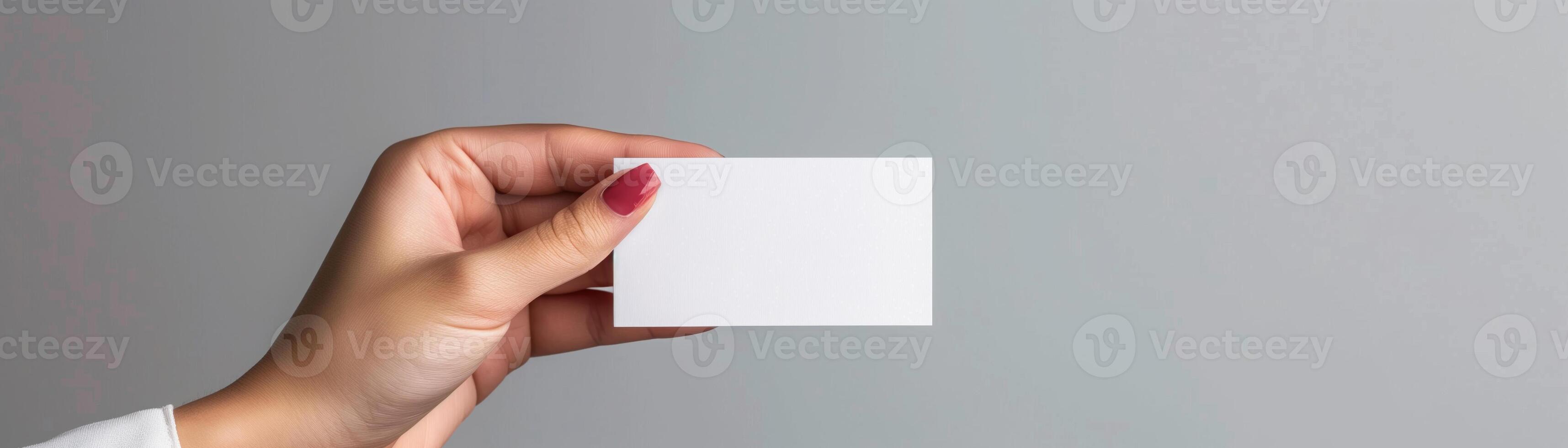 Hand holding a blank white business card against a gray background, perfect for custom text or design placement. photo