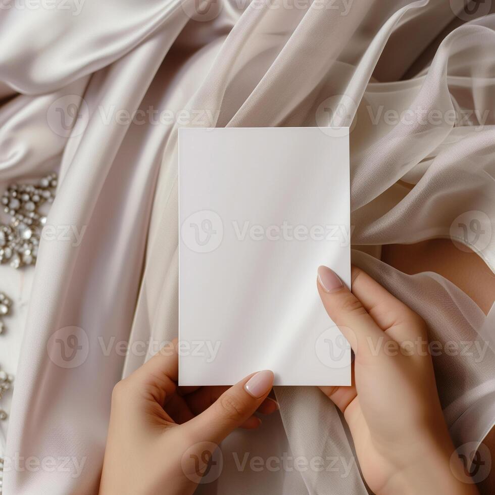 Blank paper card in female hands on the background of gentle silk fabric. photo