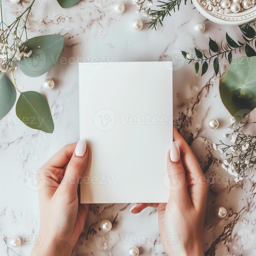 A photo of hands holding a blank notecard with a marble background and floral decorations.