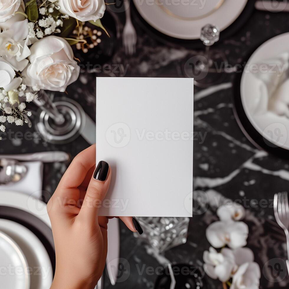 Blank paper card in hand over blurred elegant table setting background. photo
