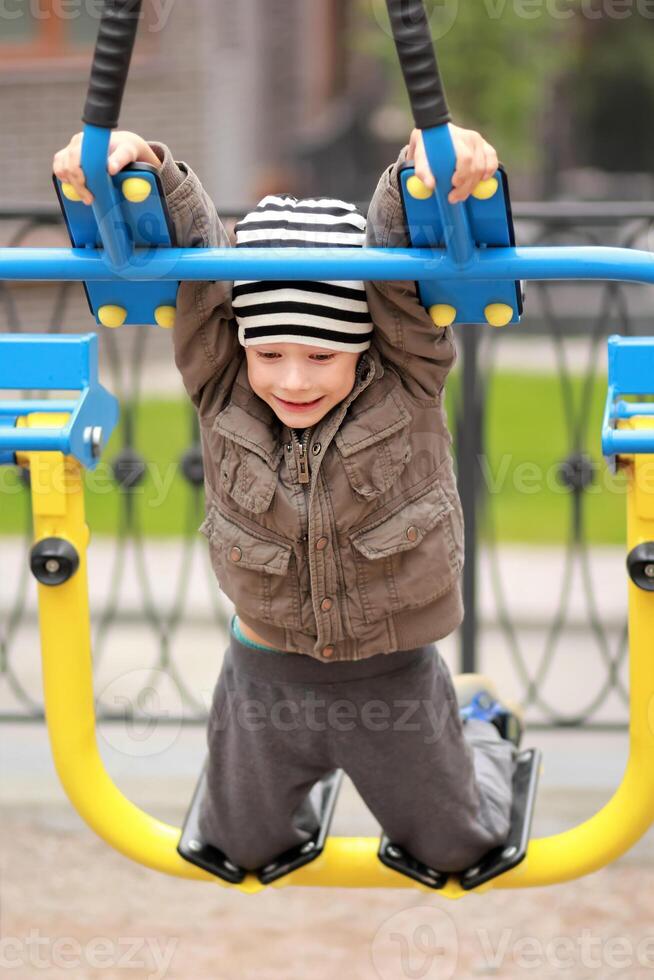 Five year old boy working out in the street, in the outdoor gym in the yard on the playground photo