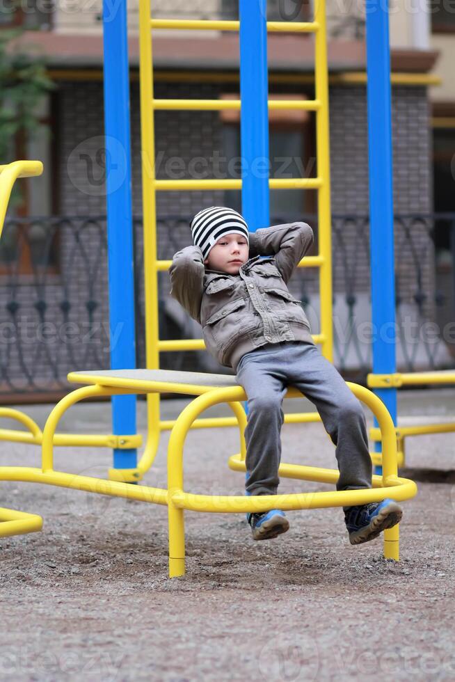 Five year old boy working out in the street, in the outdoor gym in the yard on the playground. Boy doing crunches photo