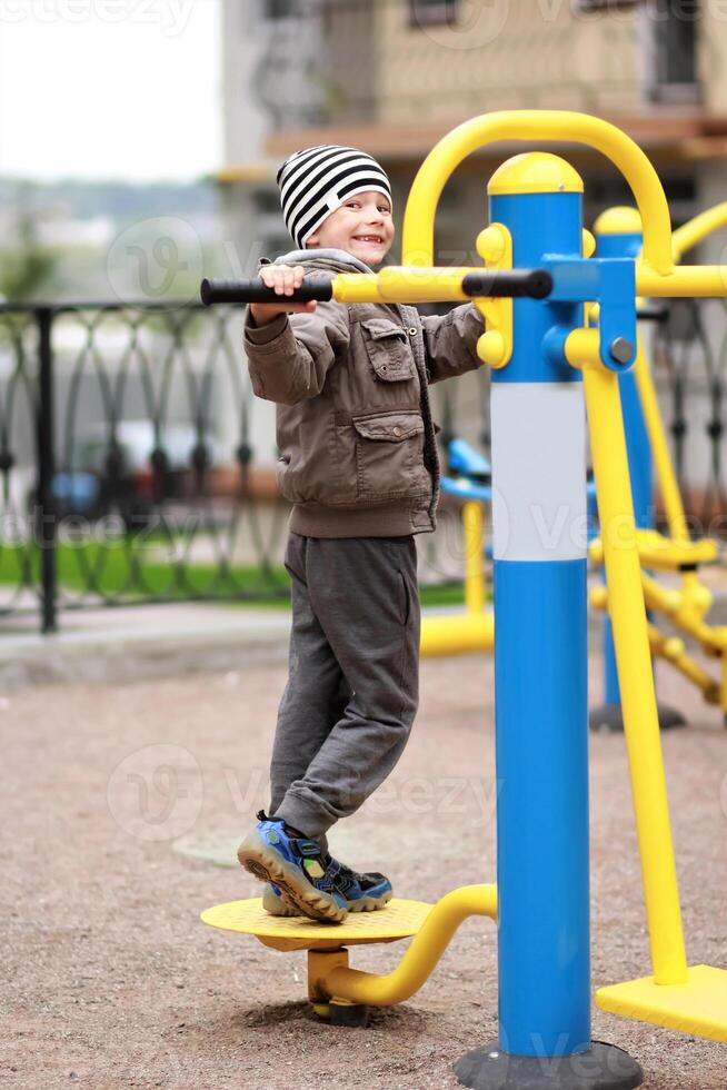 Five year old happy boy working out in the street, in the outdoor gym in the yard on the playground. Boy smiling, making faces photo