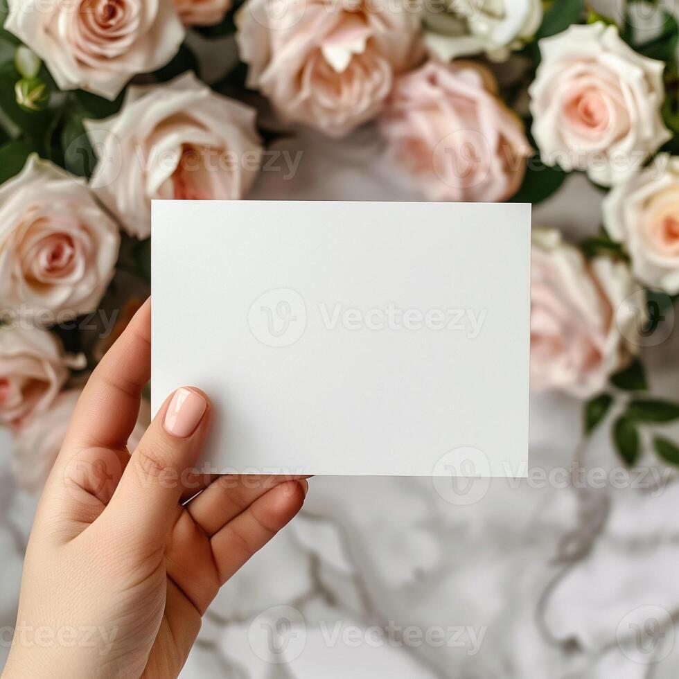 A refined mockup of a blank invitation card held over a soft bed of pastel roses, perfect for wedding or event stationery presentations. photo