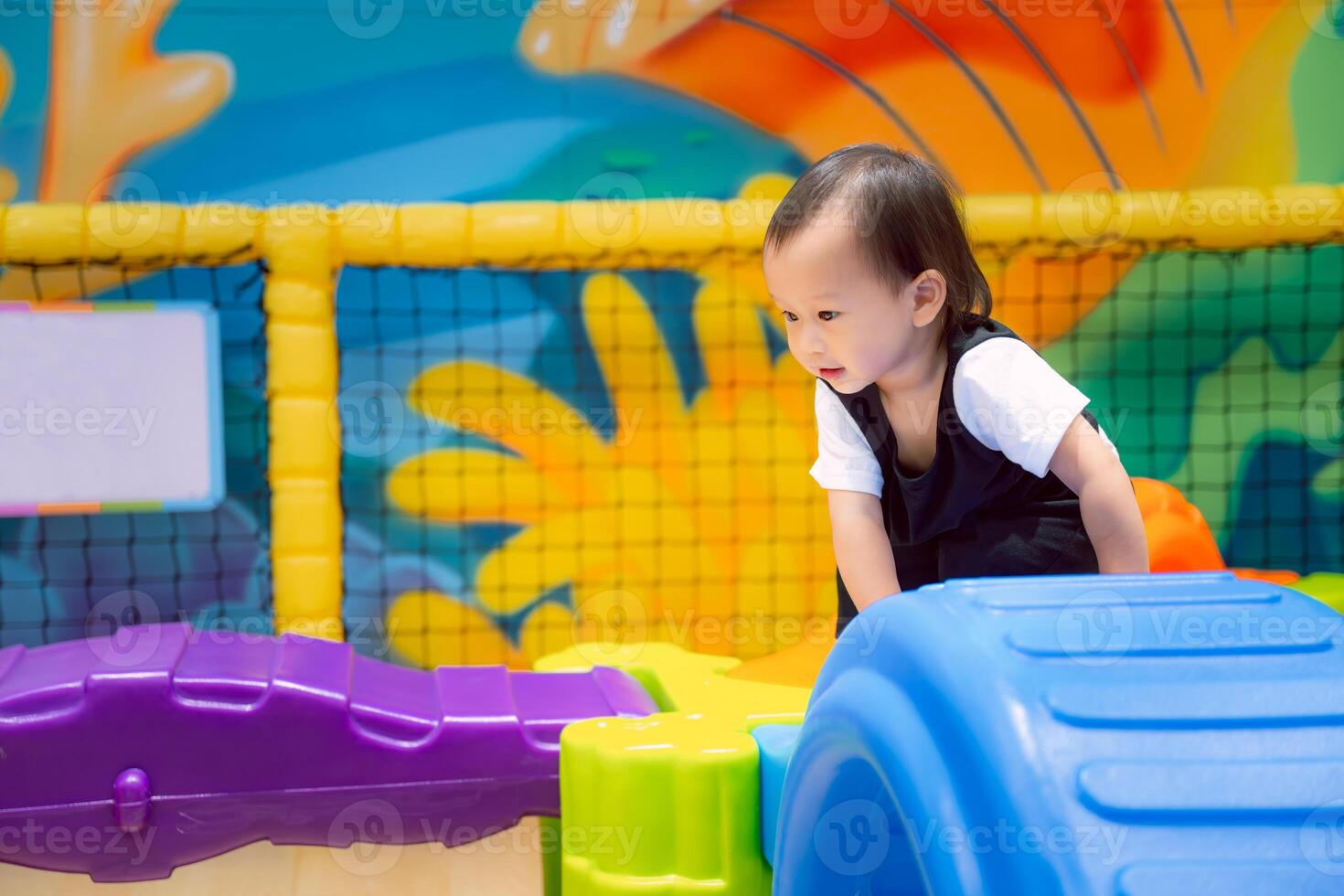 Asian little child is smiling and having fun climbing on toys in an indoor playground. Boy learning through play, leisure activities, muscle development, one year five month old kid. photo
