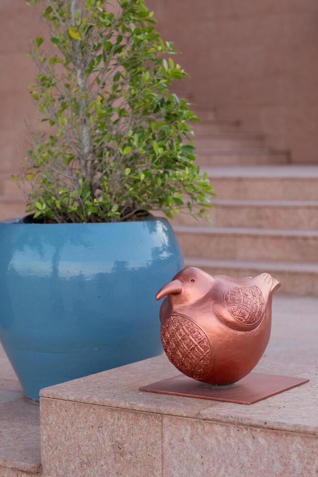 An elegant copper bird sculpture and a lush plant adorn stone steps, creating a serene atmosphere. photo