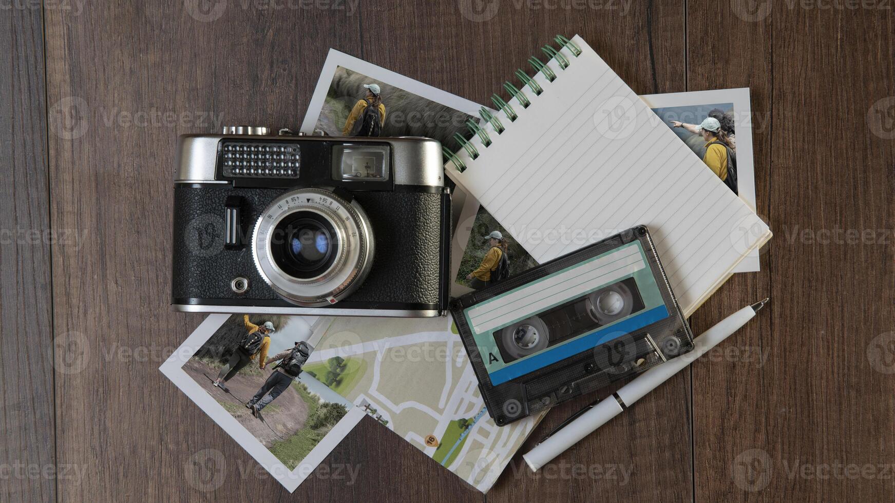 Old photo camera surrounded by photographs of women in different places, map, notebook and music cassette on a dark wooden table