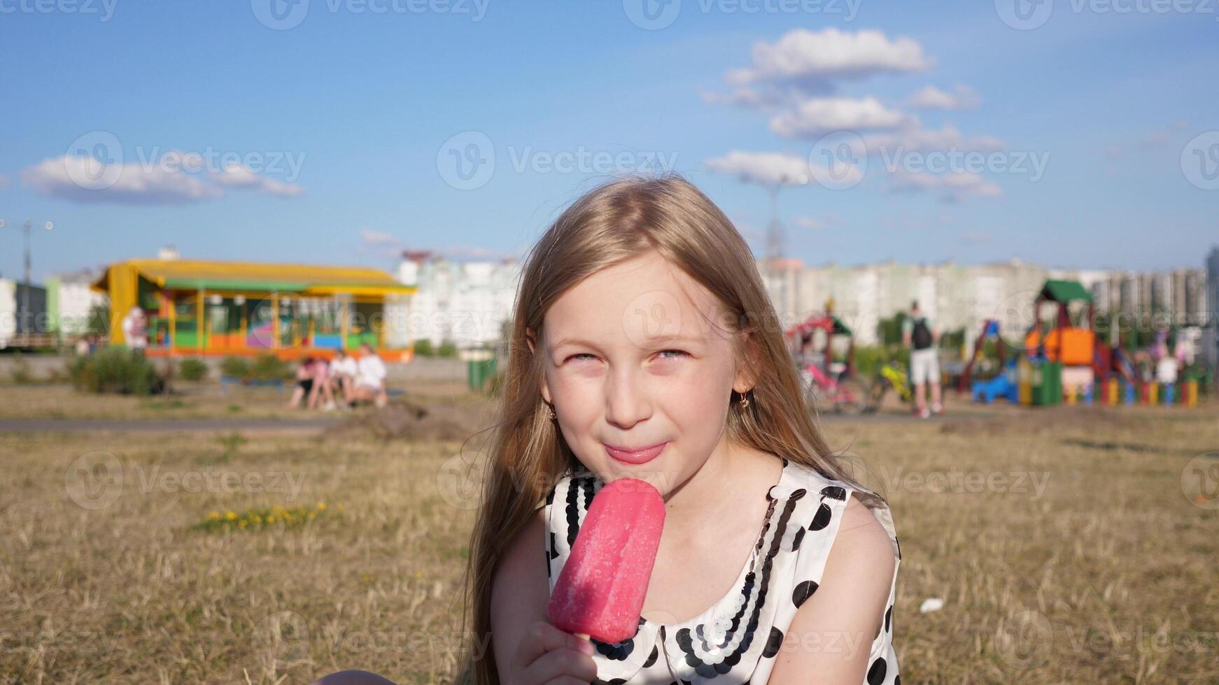 Portrait of a little beautiful Slavic girl eating ice cream in a city park in summer against the blue sky photo