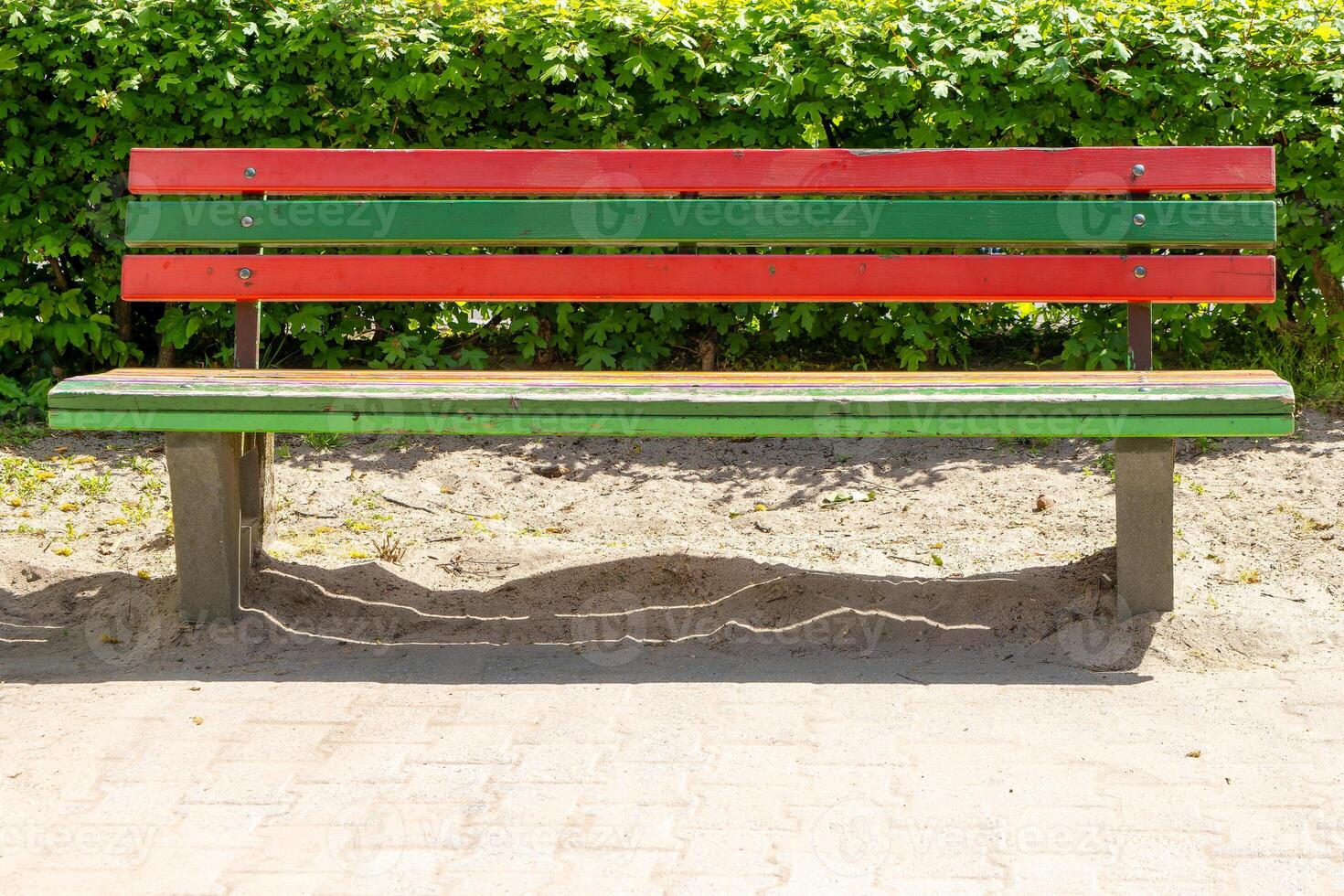 green and red bench sits in front of a hedge photo