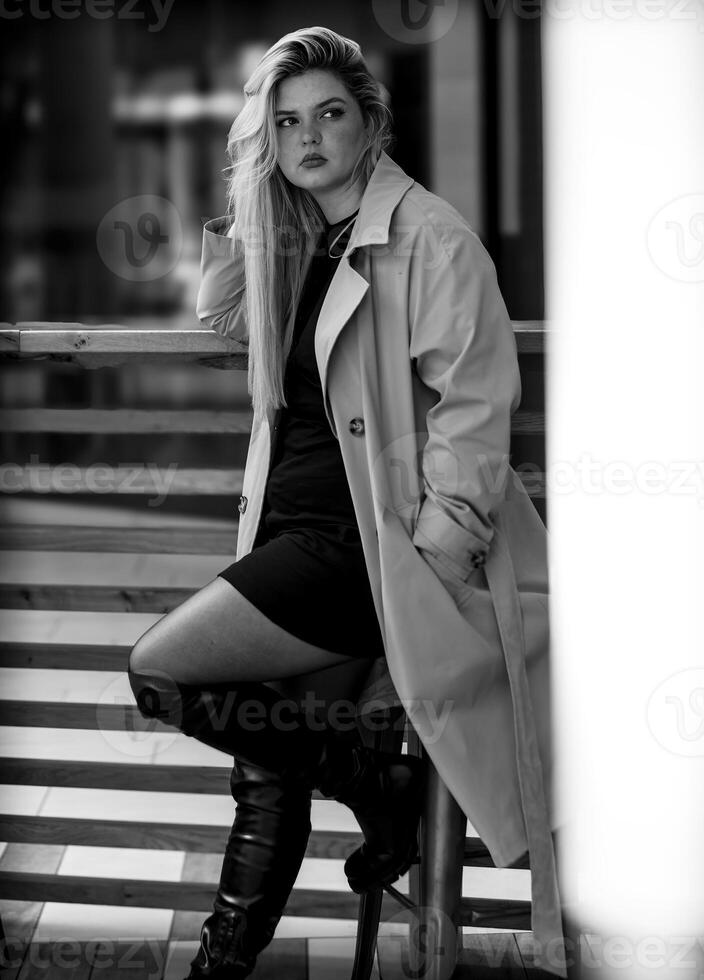attractive woman sits on a stool in the city in black and white photo
