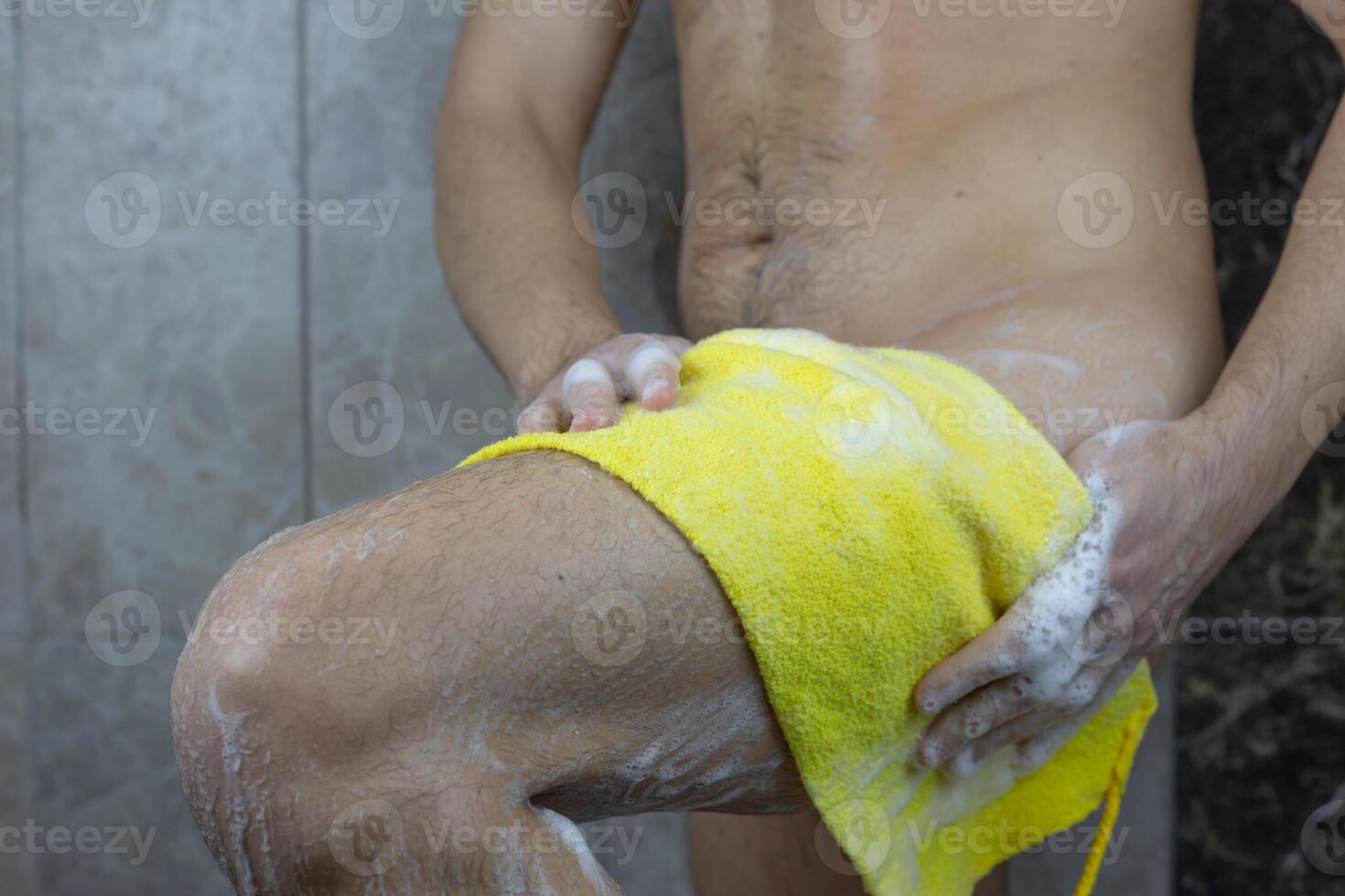Man in the shower rubs his leg with washcloth with foam, skin and body health care, cleanliness and personal care in the shower photo