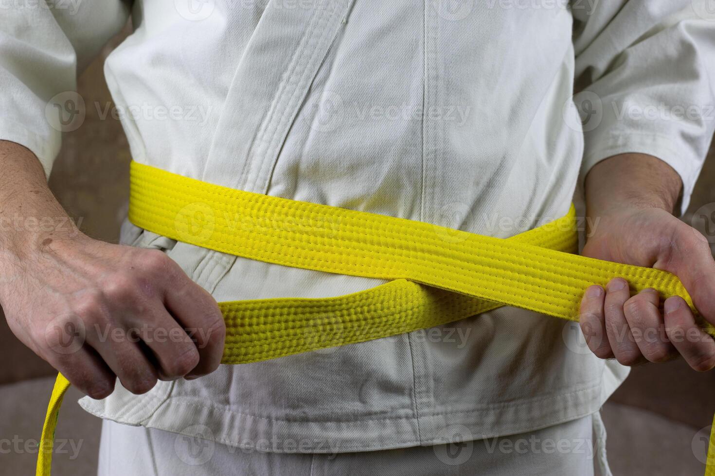 Kyokushinkai karate athlete ties yellow belt around his waist, adjusting martial arts equipment, senior student yellow belt photo