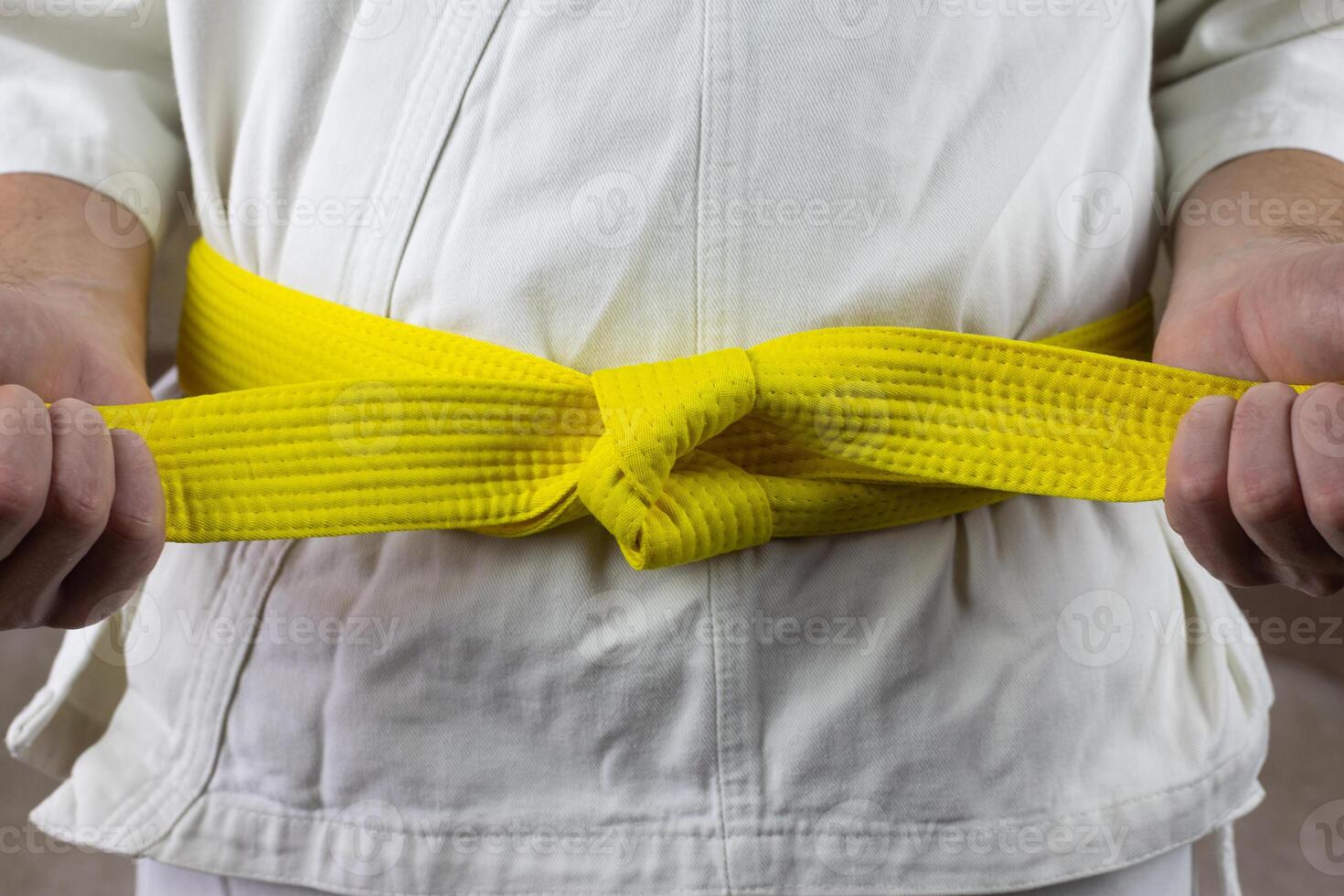Male hands tighten yellow belt in Kyokushin karate, Asian types of martial arts with belts, the sixth kyu puts belt on karate kimono photo