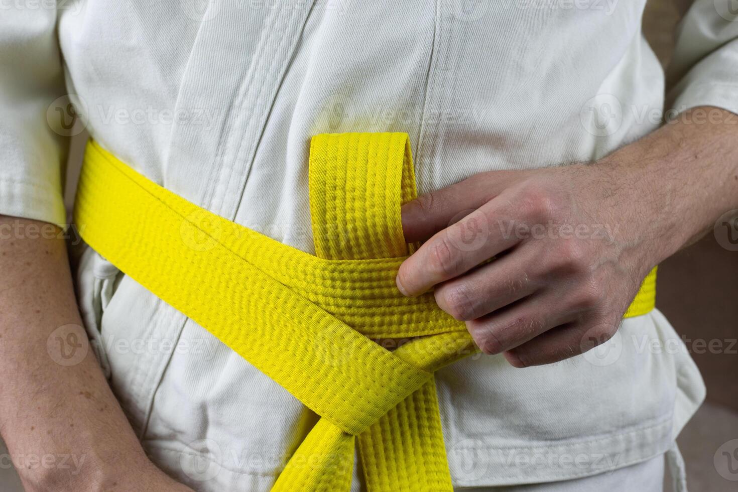 Male hands tighten yellow karate belt on kimono, close-up photo of Kyokushin karate equipment