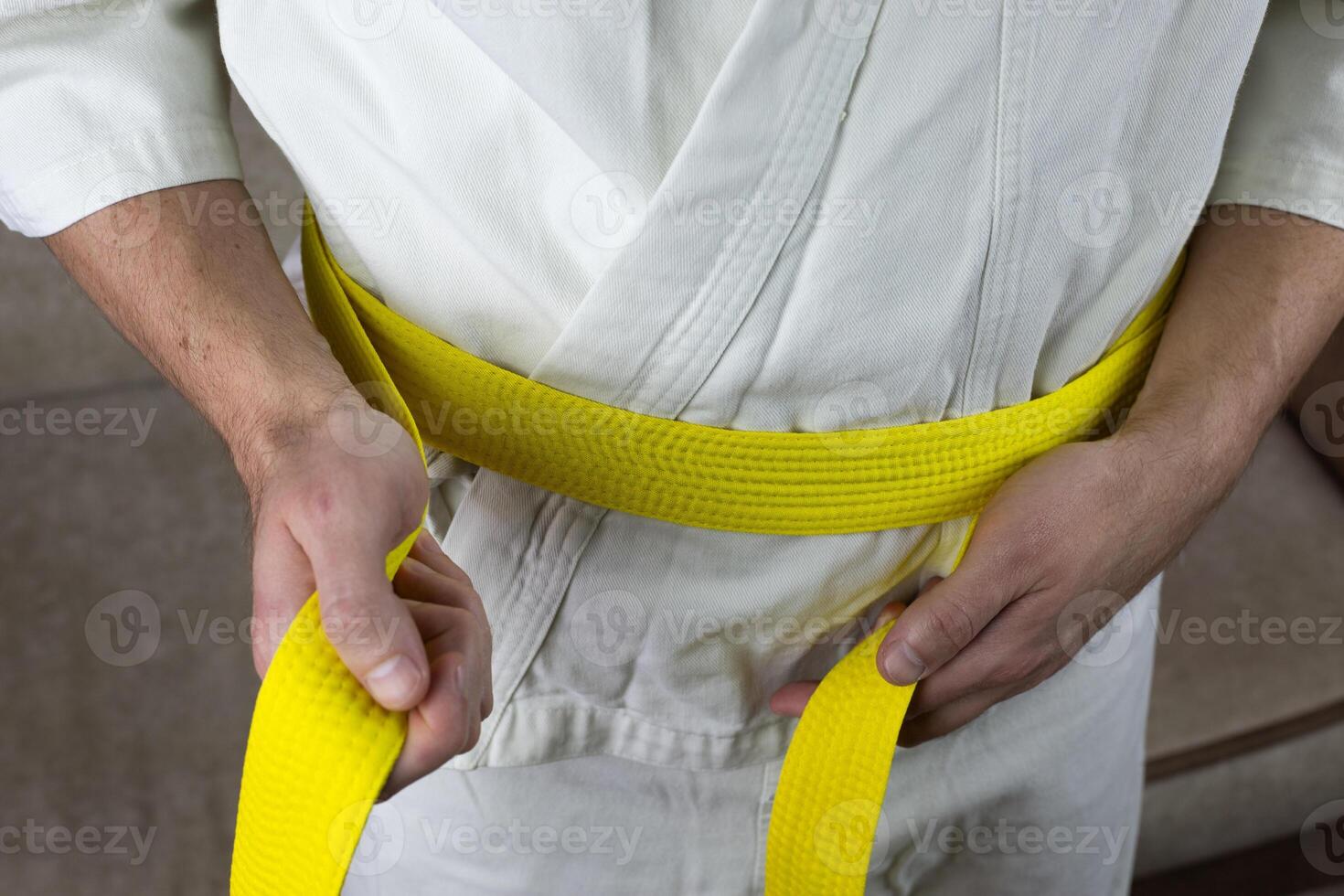 Man ties yellow Kyokushin karate belt on kimono around his waist, martial arts sports equipment before fight photo