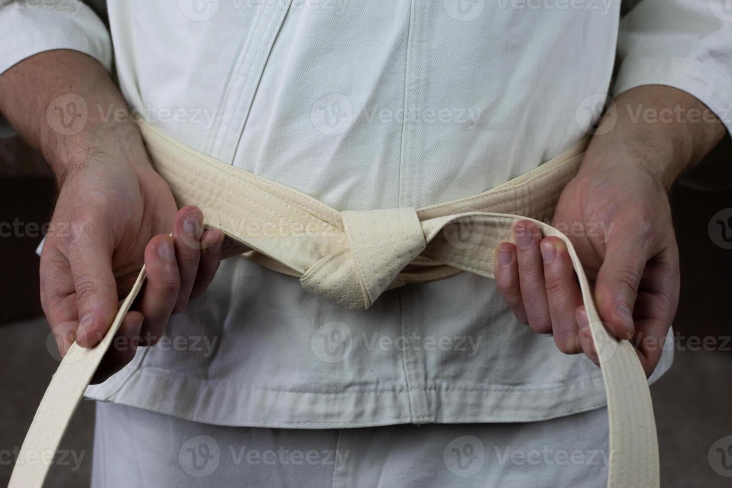 Karate athlete ties white belt on kimono, the equipment of an Asian martial arts fighter photo