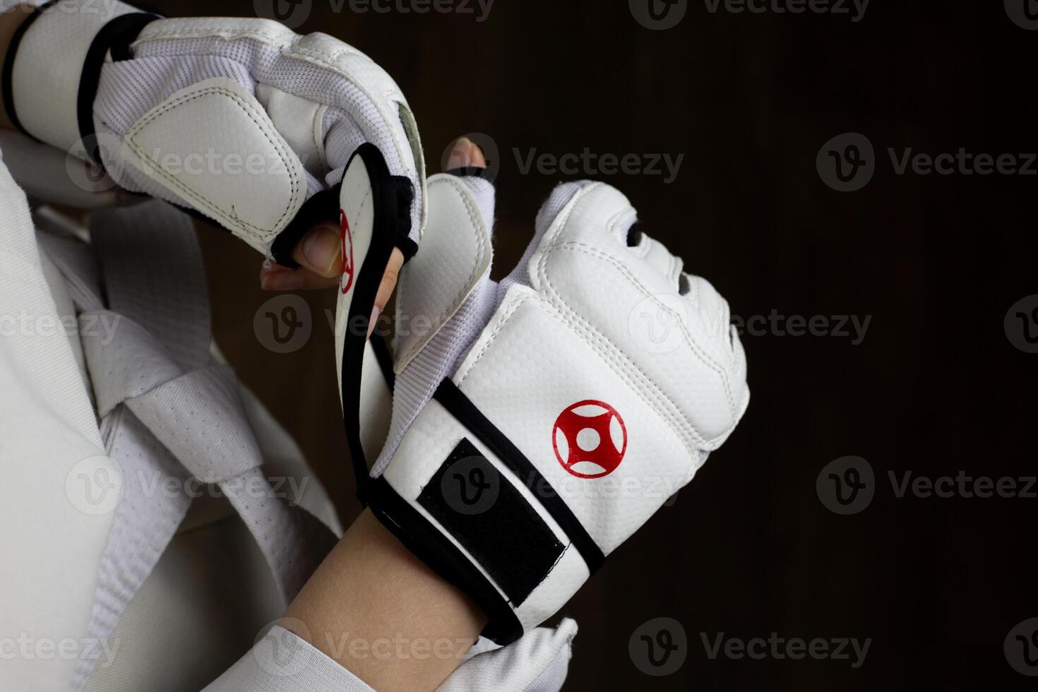 Female hands put on special Kyokushin karate fighting gloves for fight in Japanese martial arts. White karate gloves with red Kyokushinkai symbol on the athlete to protect his hands photo