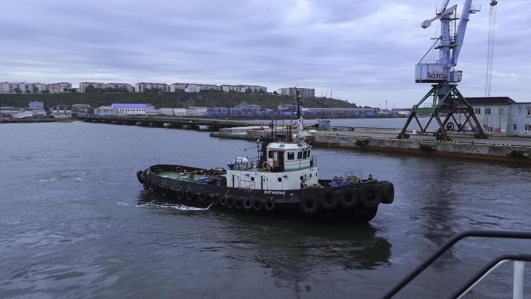 Fishing boat on background of port in cloudy weather. Clip. Fishing vessel sails out of seaport into sea. Fishing boat sails into sea on cloudy day photo