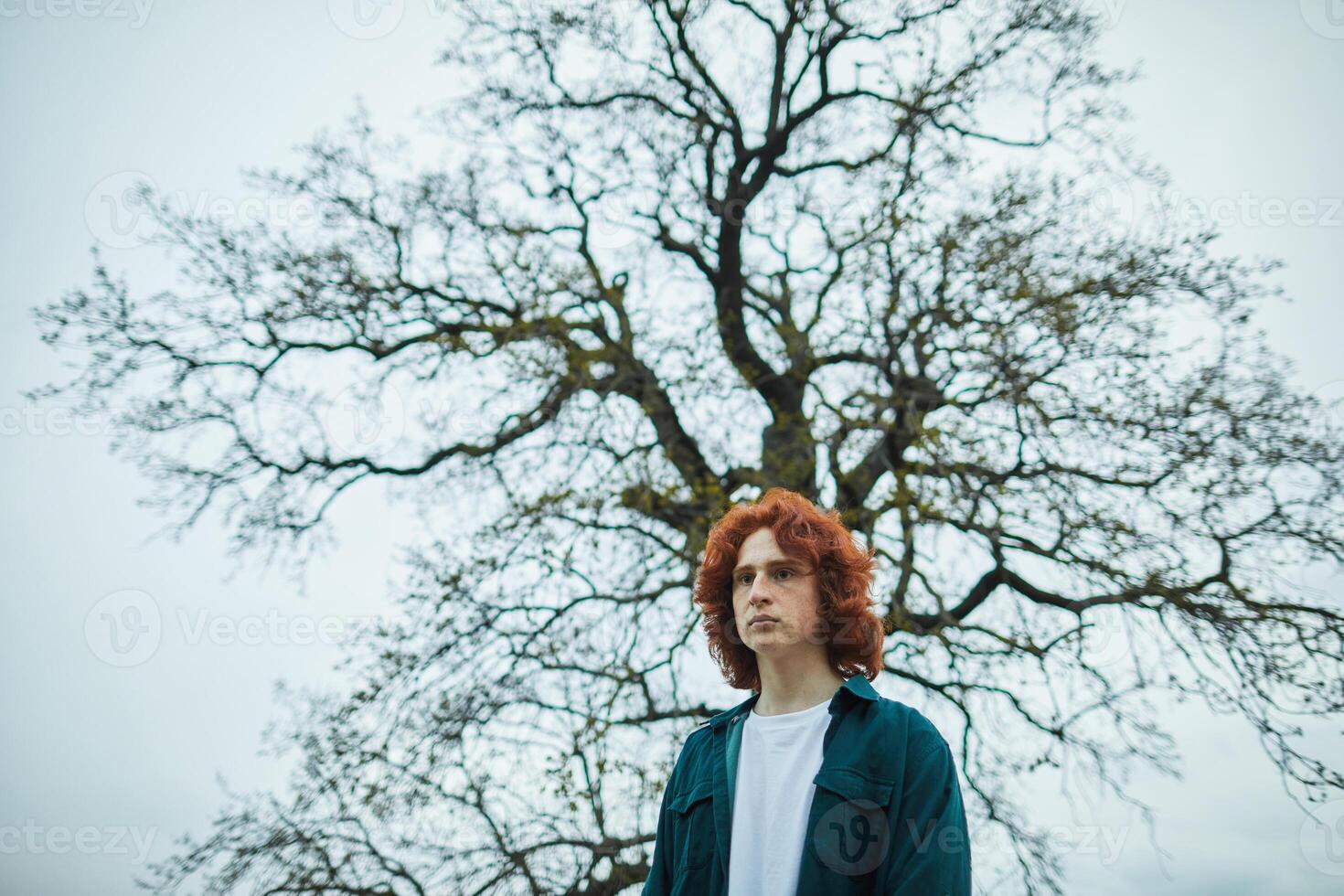 a man with red hair standing in front of a tree photo