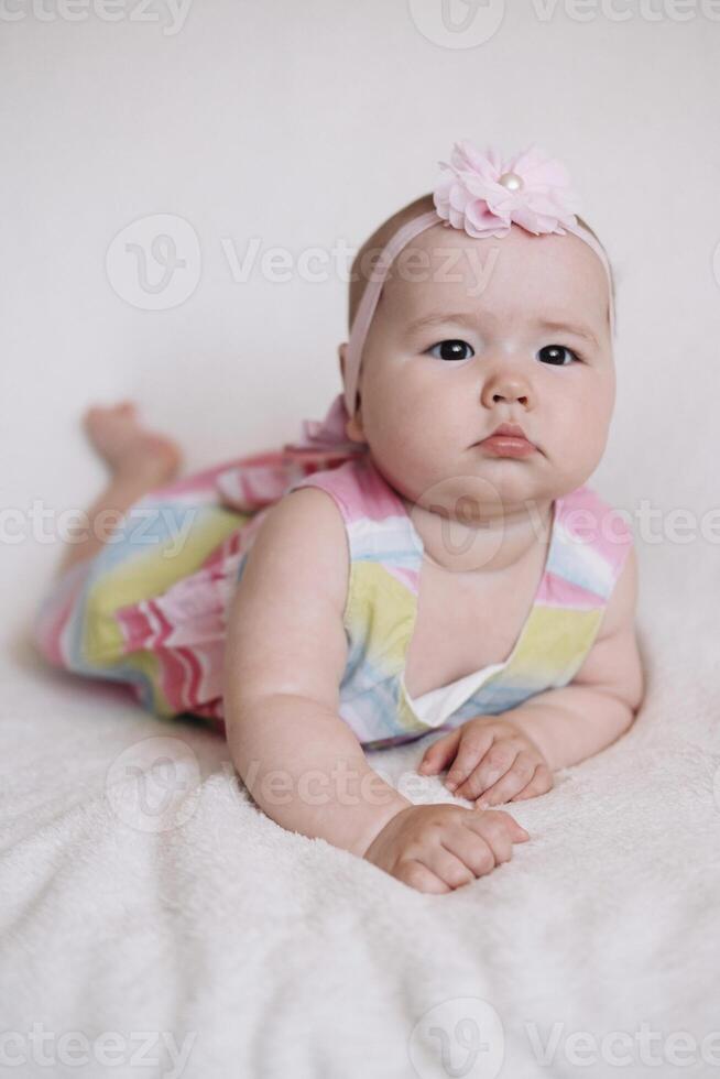 Full body figure of an infant looking at the camera while lying on his back on a white sheet bed photo