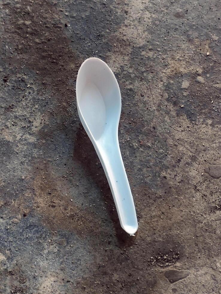 Single white plastic spoon lying on rough floor photo