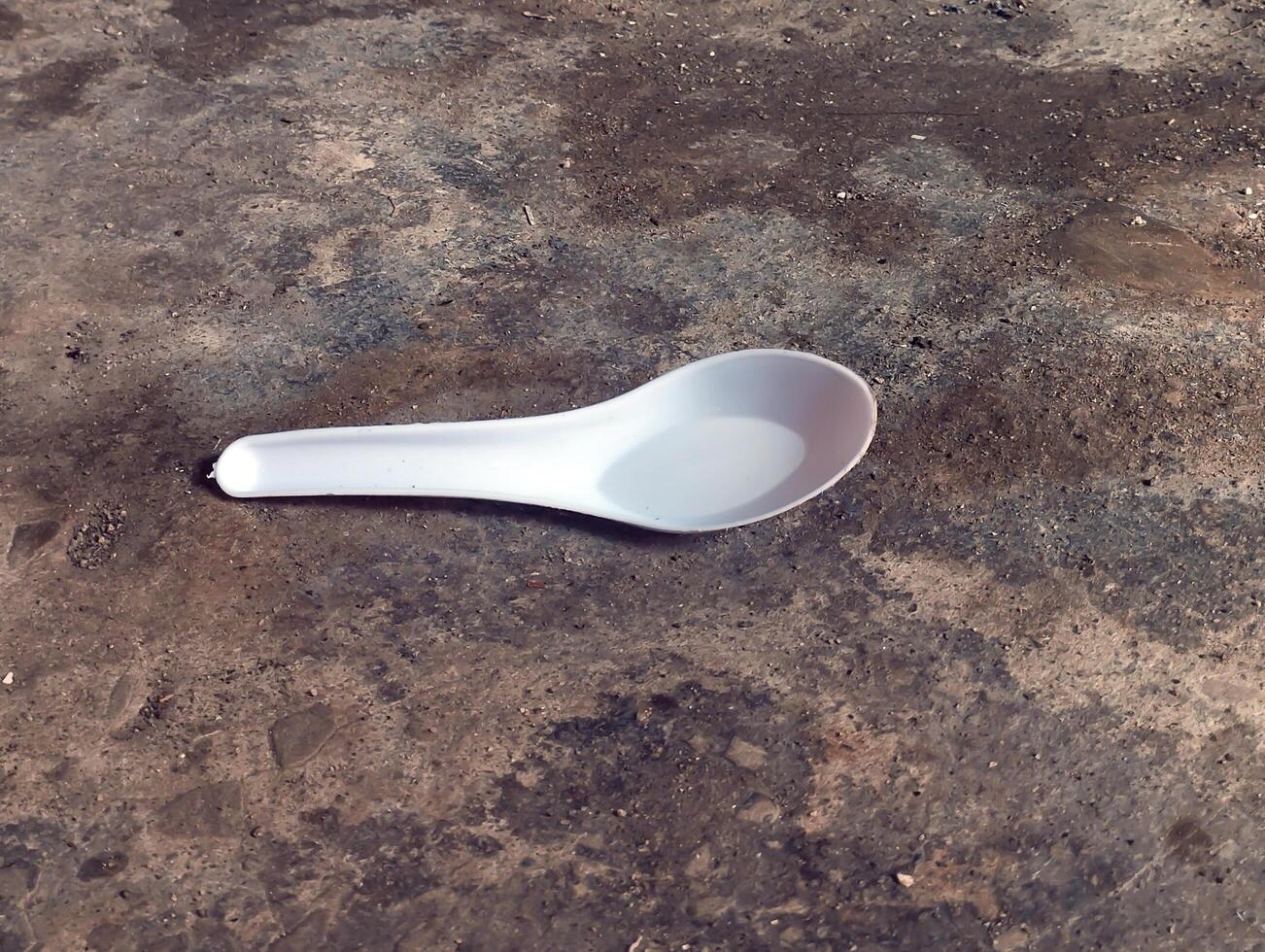 Single white plastic spoon lying on rough floor photo