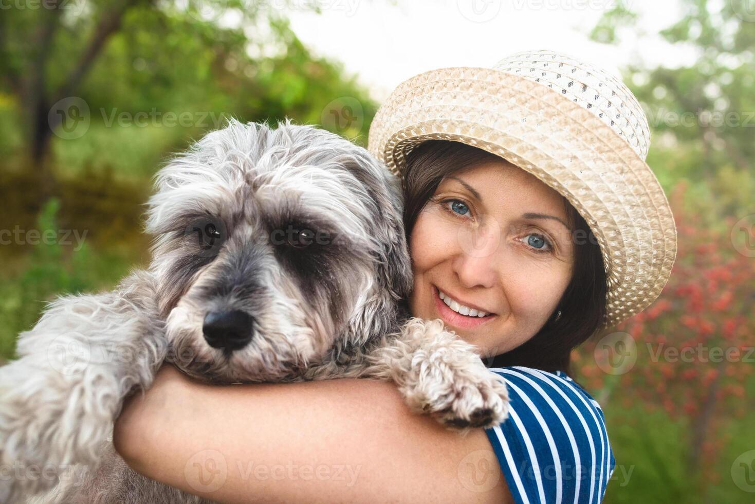 Image of beautiful middle-aged woman wearing straw hat looking aside while walking in summer park photo