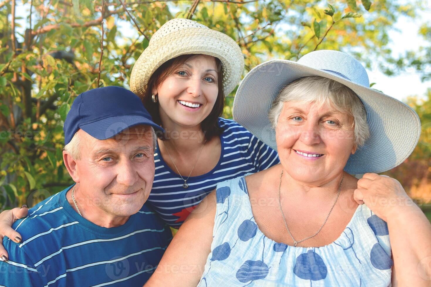 Beautiful old couple is sitting on the bench in the park with their adult daughter. Grandma and grandpa are hugging and smiling. Real love and family relationship photo. Generations concept. photo