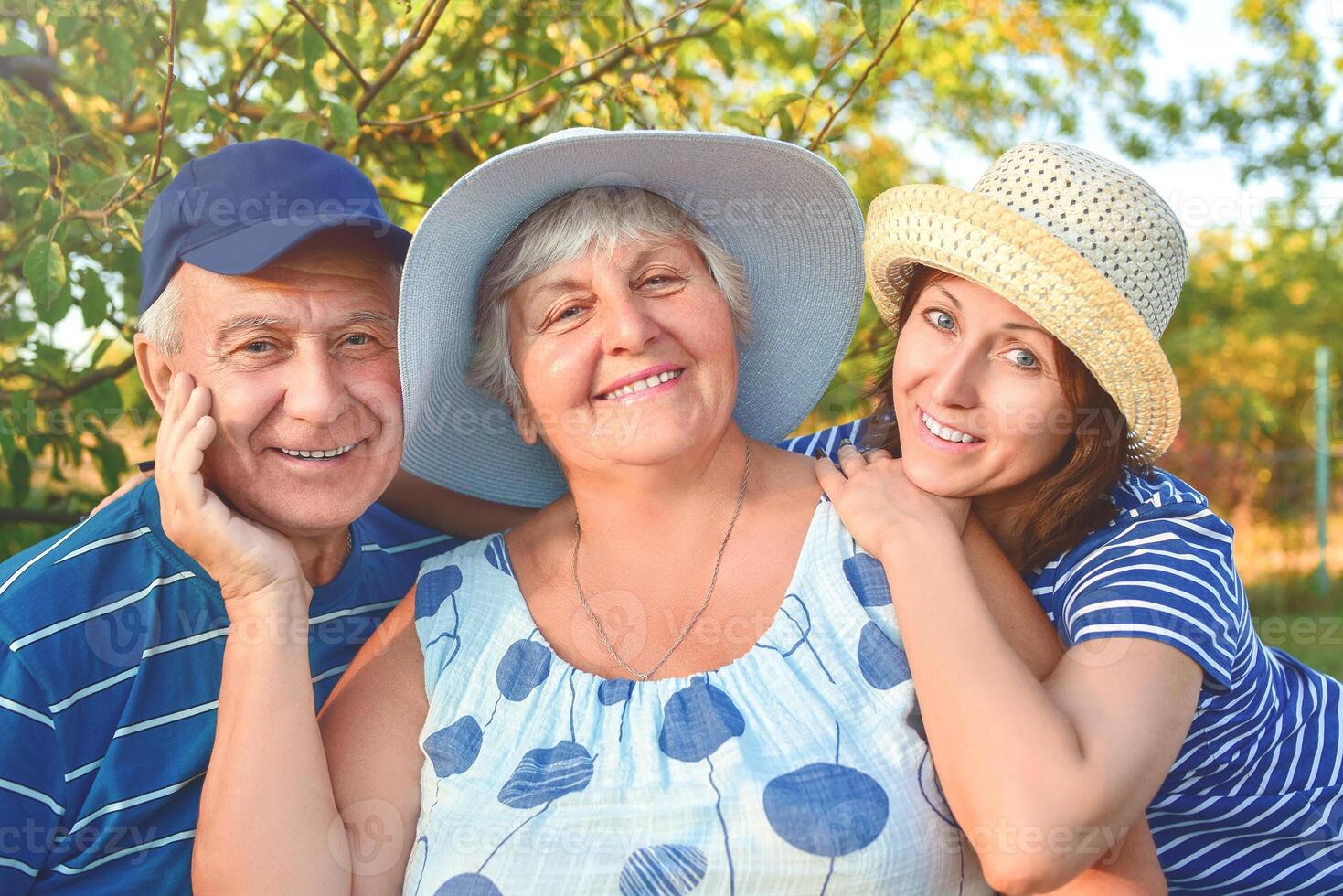 Beautiful old couple is sitting on the bench in the park with their adult daughter. Grandma and grandpa are hugging and smiling. Real love and family relationship photo. Generations concept. photo